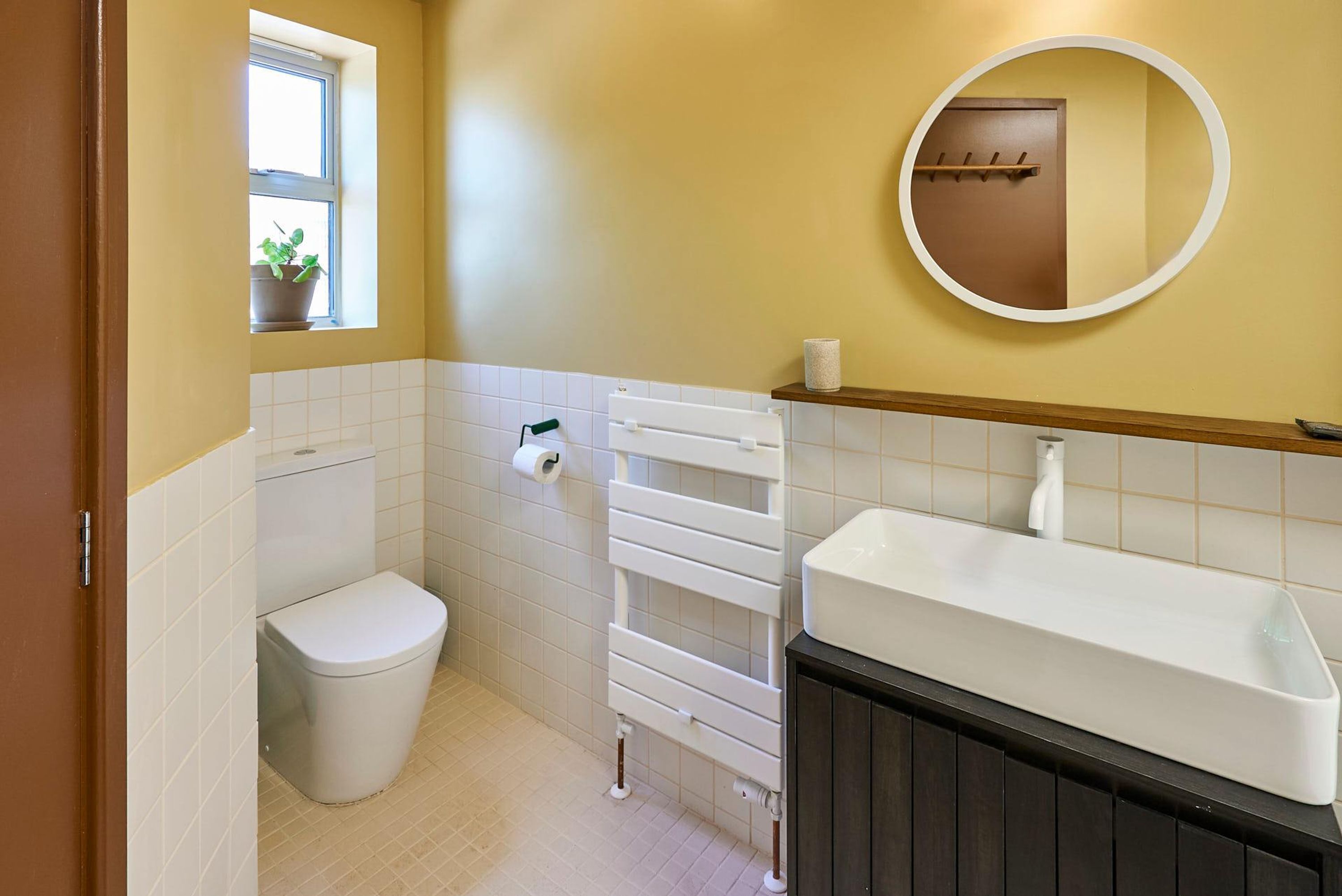 Une salle de bain avec des toilettes, un lavabo blanc, un porte-serviettes et une fenêtre avec une plante.