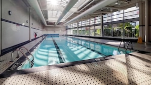 An indoor swimming pool with clear glass walls, a tiled floor, and a skylight ceiling. - Modern Central Location with Sauna Jacuzzi & Pool (Vancouver)