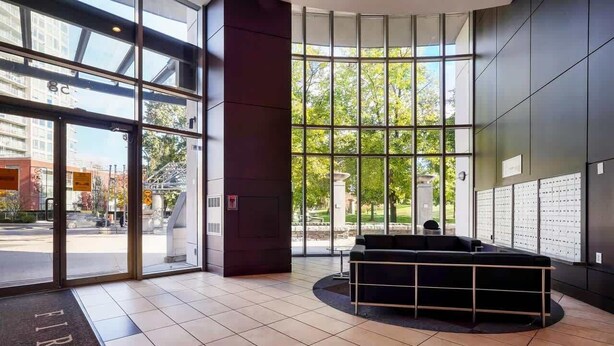 A modern lobby with large windows, a reception desk, and a seating area. - Modern Central Location with Sauna Jacuzzi & Pool (Vancouver)