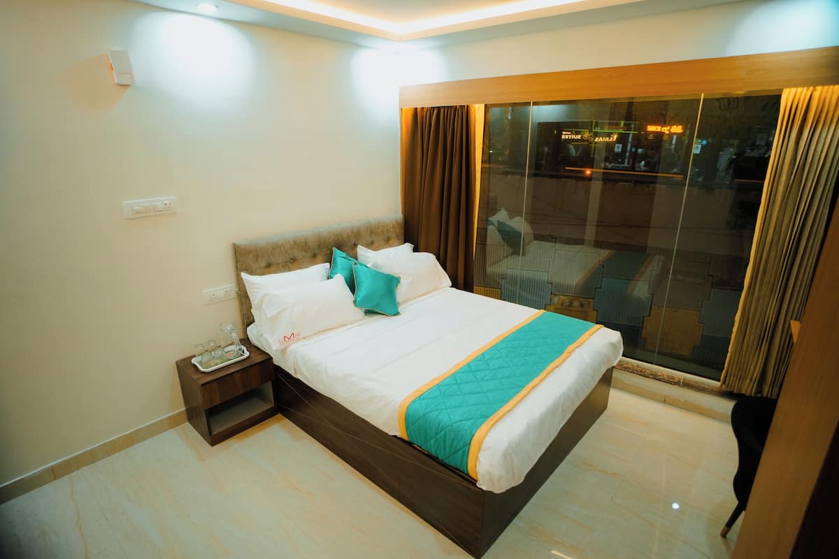 Habitación de hotel con una cama grande, una mesita de noche, un balcón con paredes de vidrio y vistas a la ciudad.