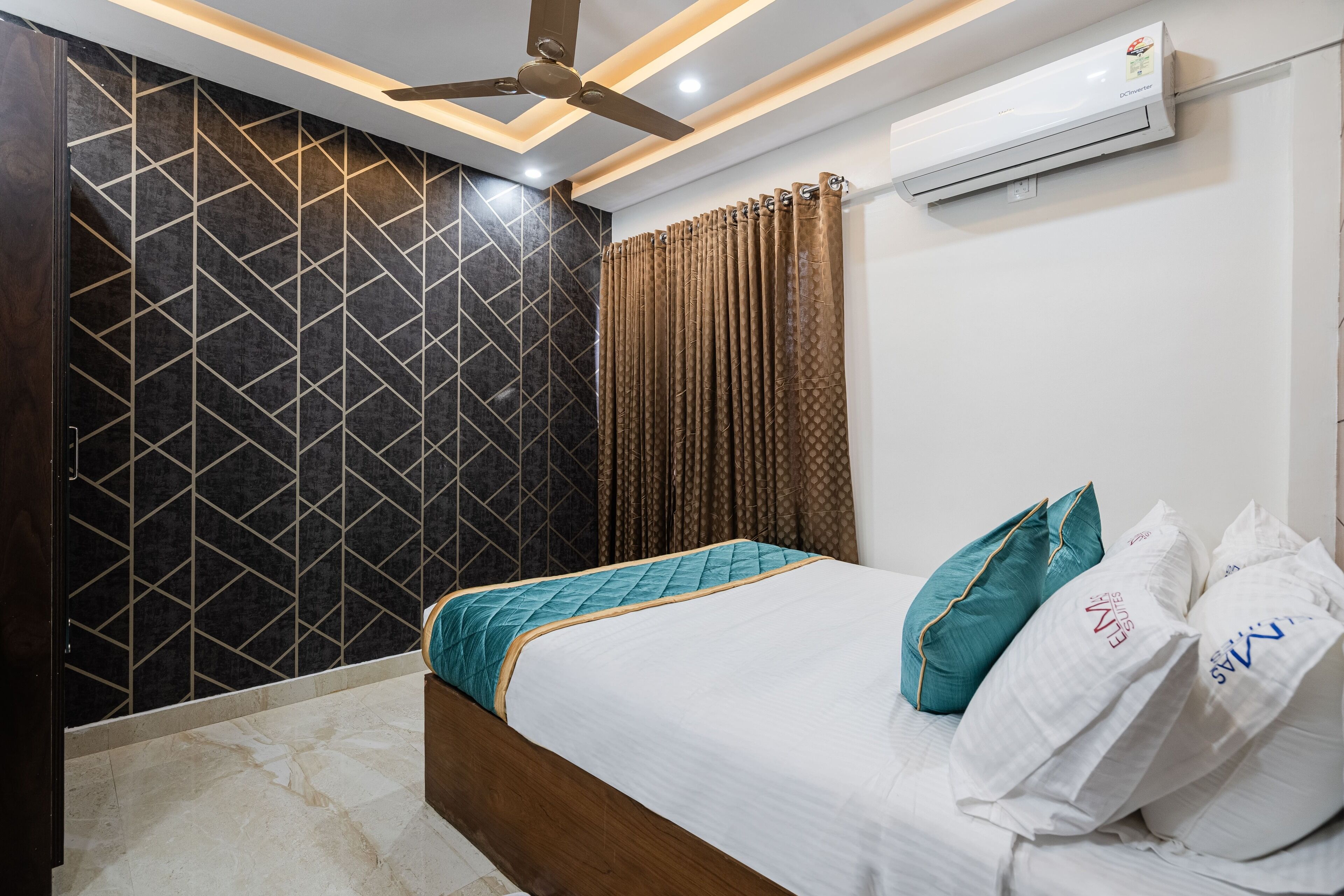 A hotel room with a bed, a ceiling fan, an air conditioning unit, and a patterned wall.