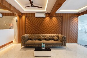 A modern lobby with a tufted sofa, a ceiling fan, and a patterned wall. - Elmas Suites - Bellandur (Bengaluru)