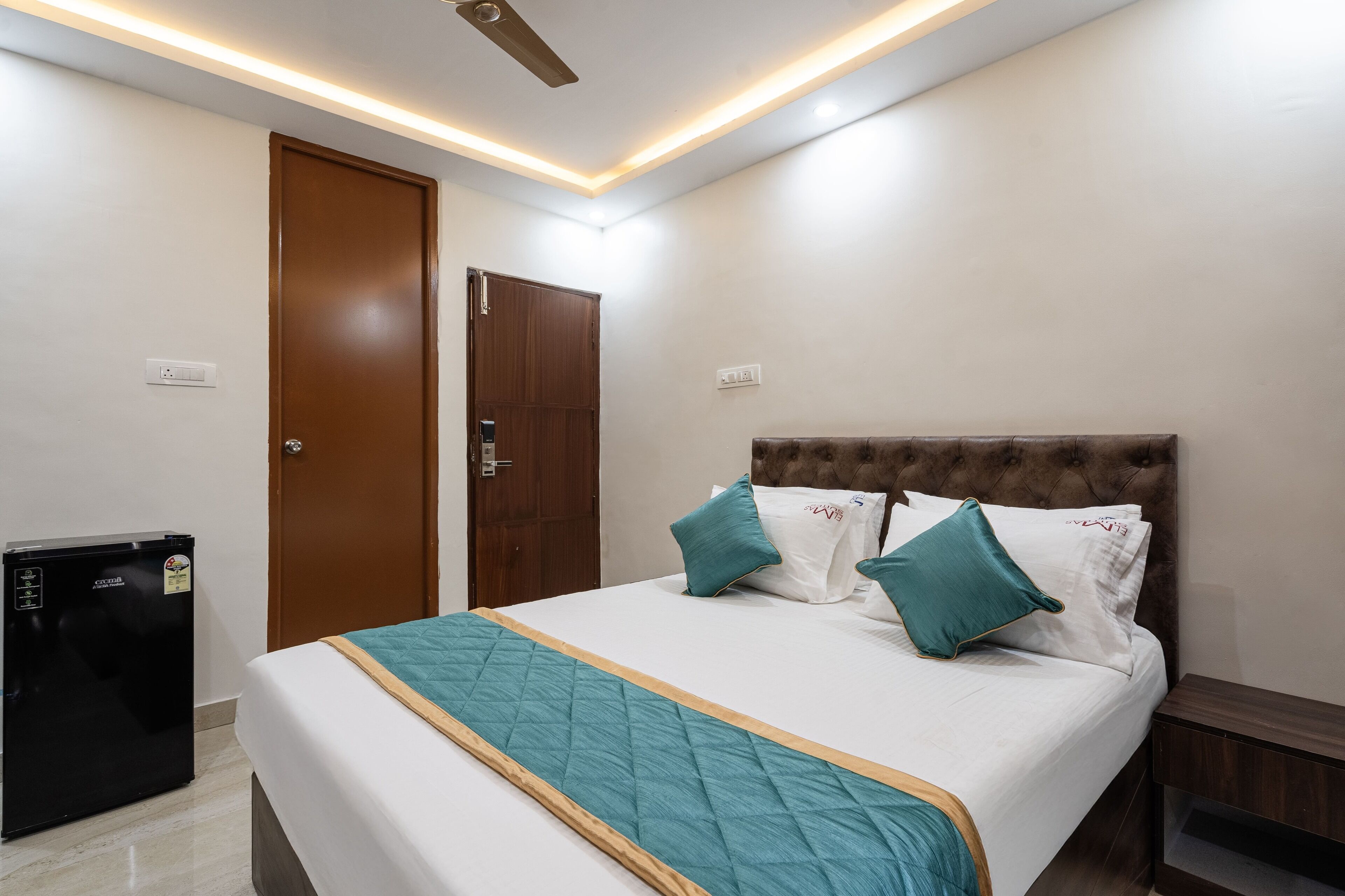 A neatly arranged hotel room with a bed, a small refrigerator, and a door.