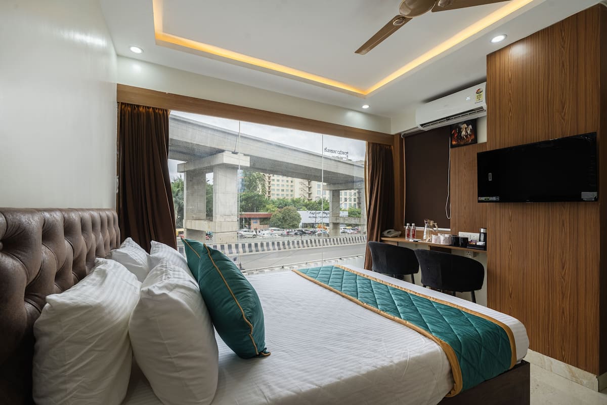 Habitación de hotel con cama, escritorio, silla, televisor y vista a la ciudad.