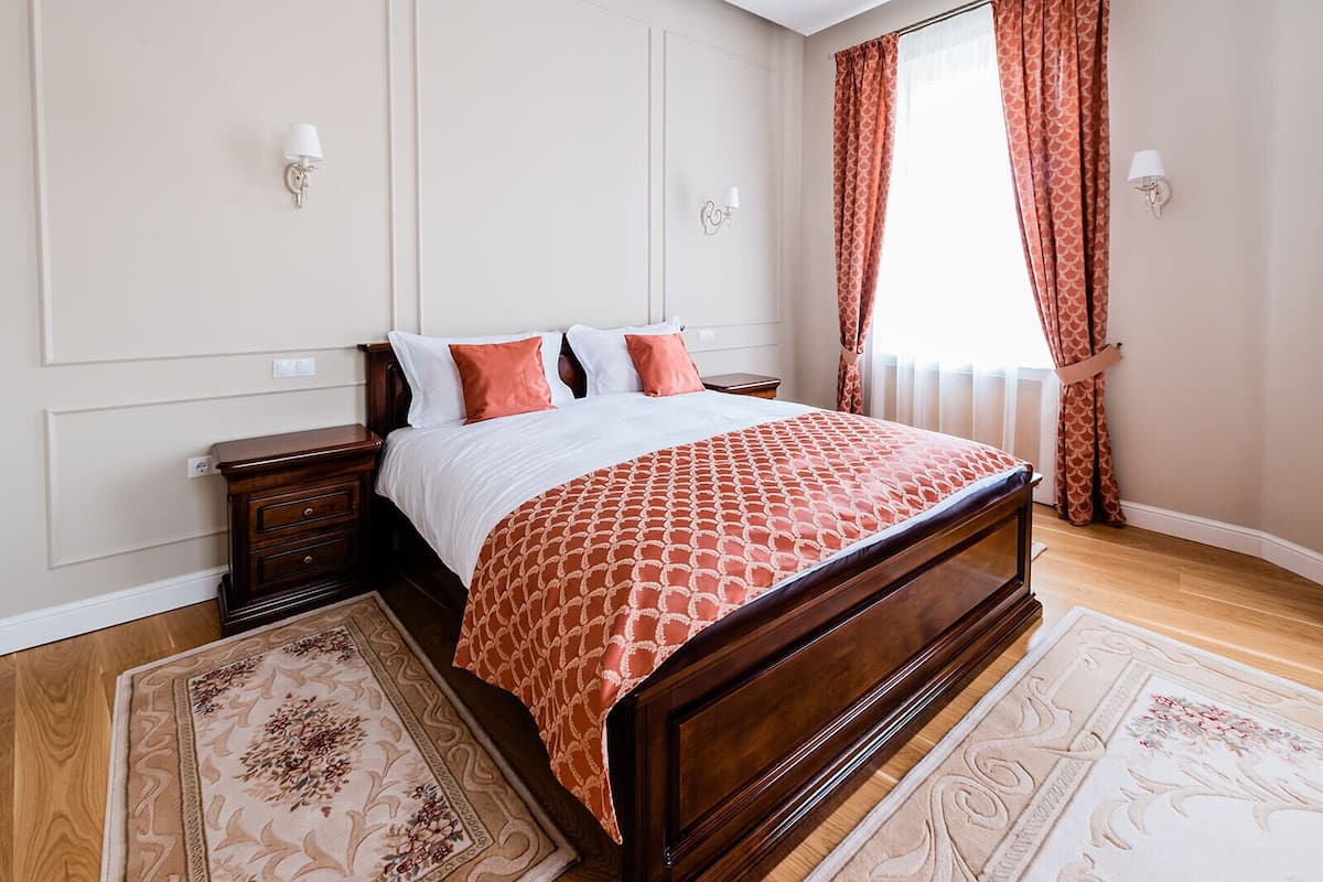 A bedroom with a wooden bed, white and red bedding, a nightstand, a dresser, and patterned rugs.