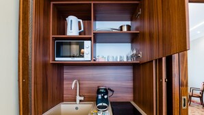 A compact kitchenette with a microwave, kettle, and electric kettle on shelves, a sink with a faucet, and a Bosch coffee maker. - Casa Petra (Sibiu)