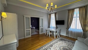 A modern living room with a dining area, wooden flooring, a chandelier, and a large window with curtains. - Casa Petra (Sibiu)