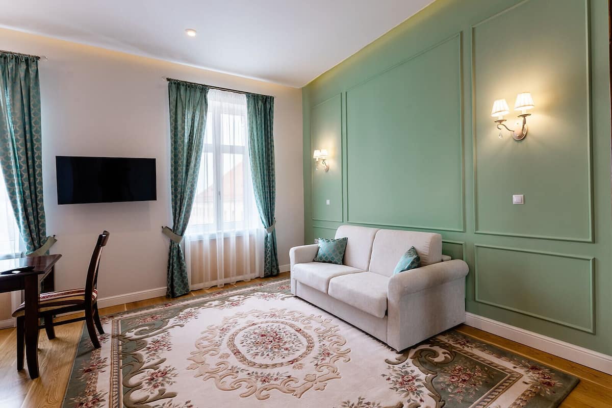 A living room with a sofa, a TV mounted on the wall, a dining table with chairs, and a large floral rug.