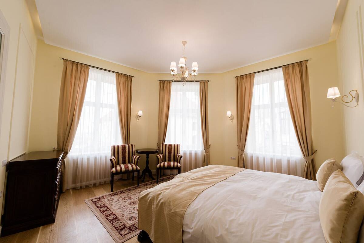 A hotel room with a large bed, two armchairs, a small table, and a chandelier.