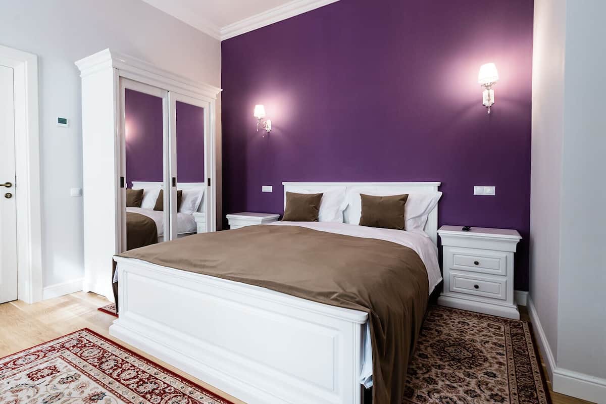 A bedroom with a large bed, two bedside tables, a nightstand, a wardrobe, and a patterned rug.