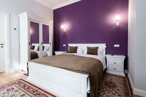 A bedroom with a large bed, two bedside tables, a nightstand, a wardrobe, and a patterned rug. - Casa Petra (Sibiu)