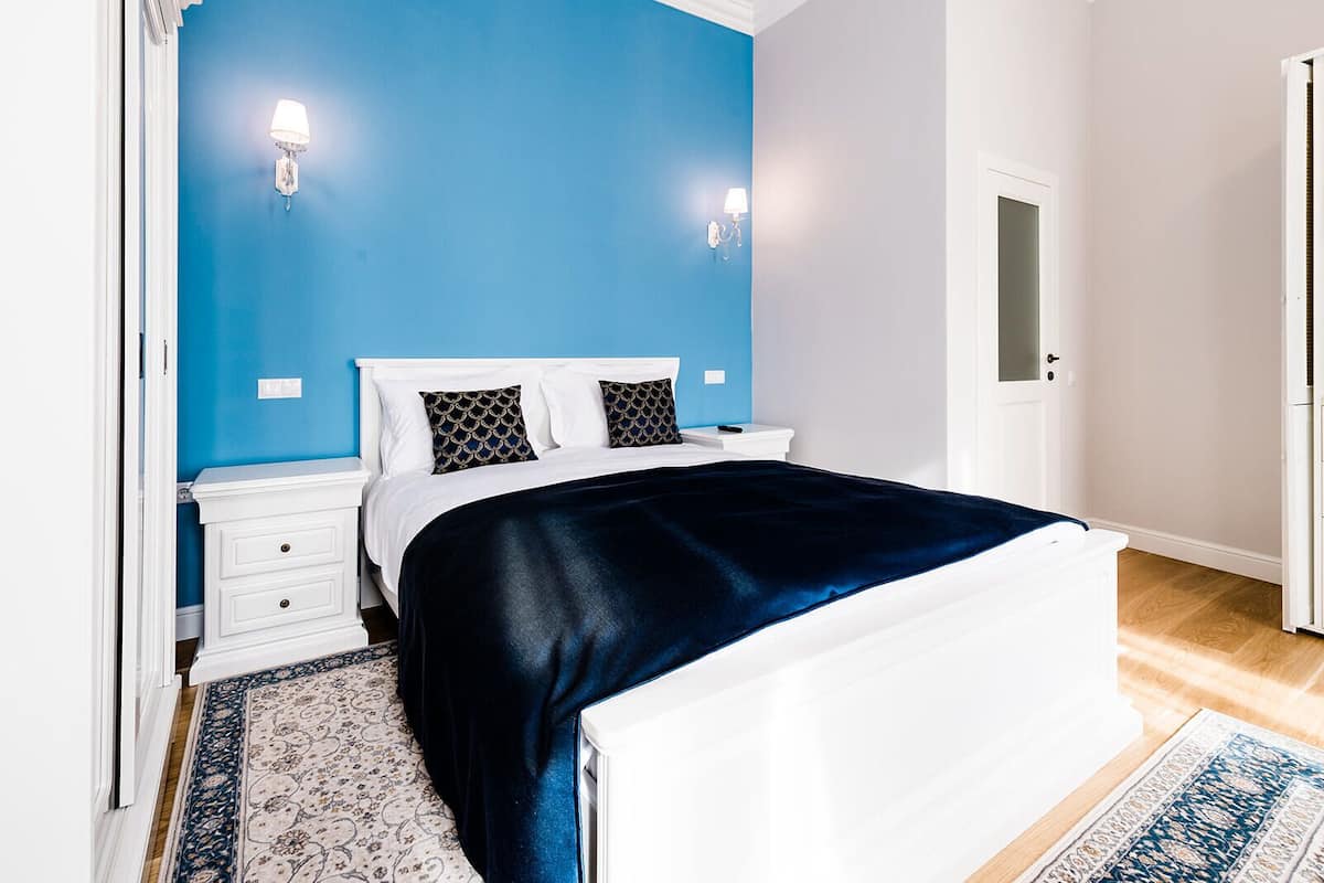 A bedroom with a bed, white nightstands, a blue accent wall, and a patterned rug.