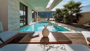 Area piscina moderna con pavimento in legno, poltrona prendisole e vista mare e montagne.