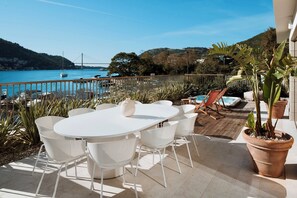 An outdoor patio with a white table and chairs, a potted plant, and a view of a bridge and water. - Villas & Spa Dubrovnik (Dubrovnik)