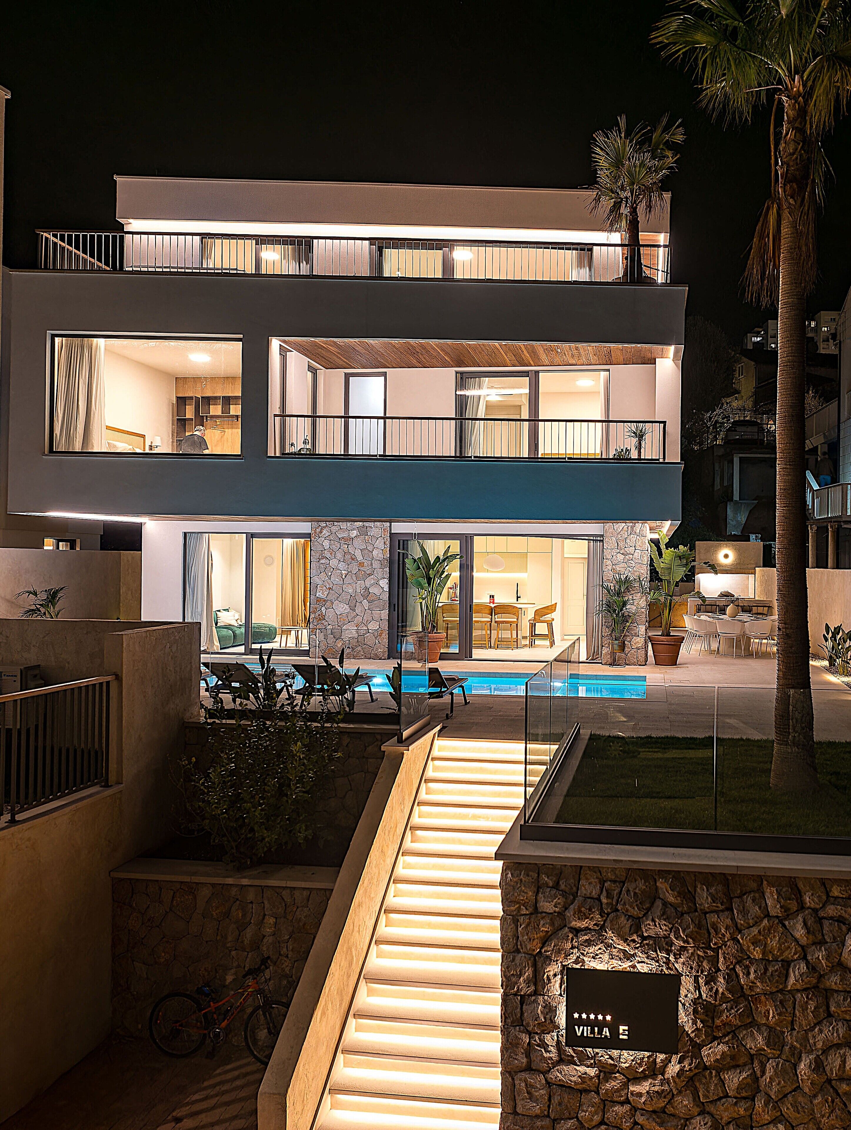 A modern two-story villa with a swimming pool, outdoor seating, and a stone facade.