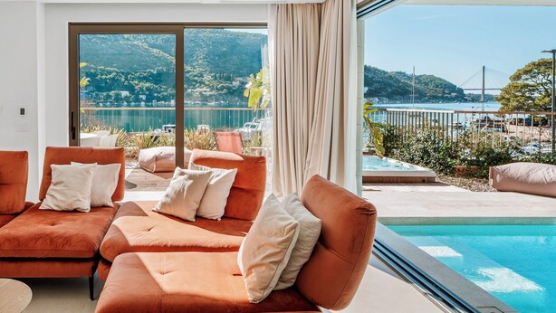 Un soggiorno moderno con divani arancioni e una grande finestra che si affaccia su una piscina e un panorama suggestivo di colline e un ponte.