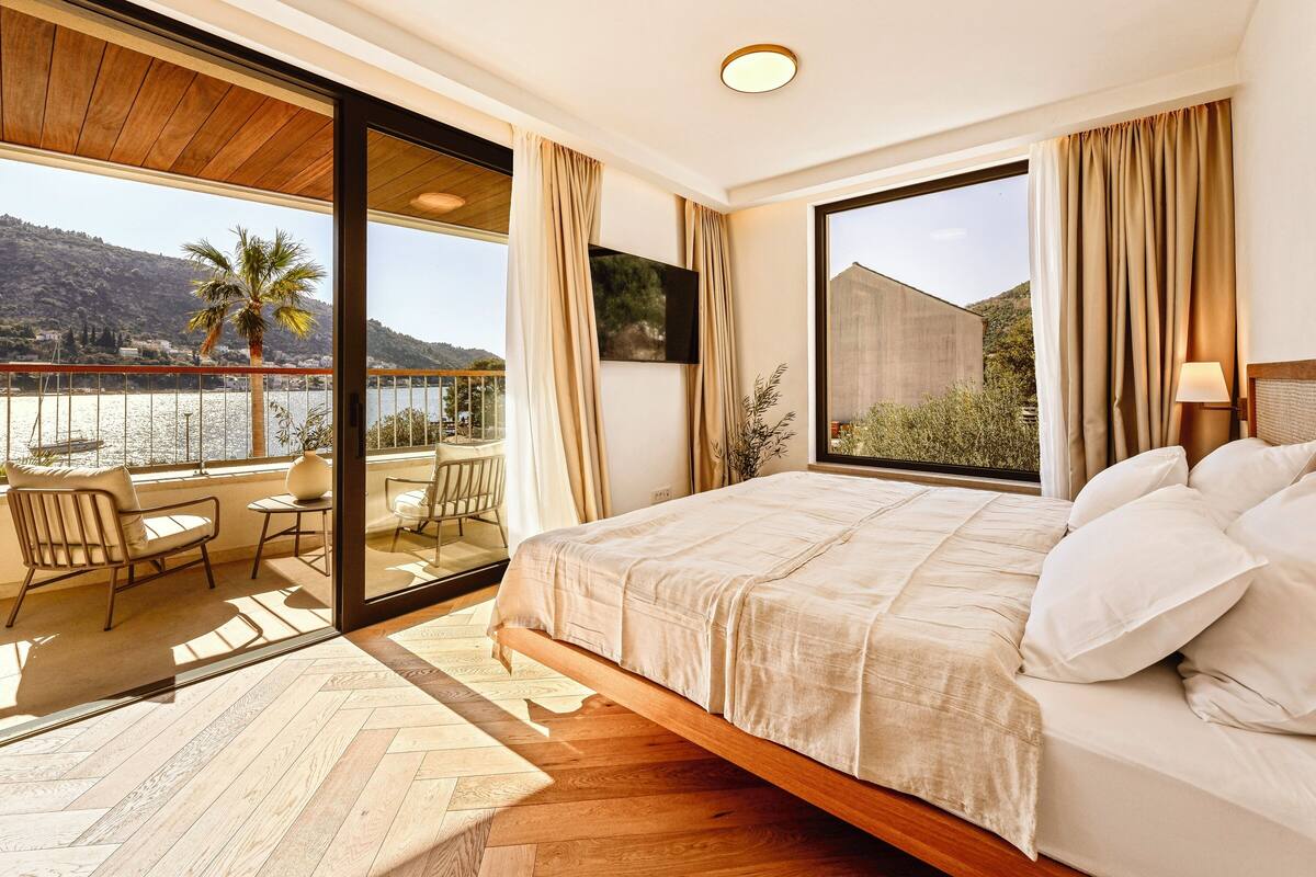 Une chambre avec un grand lit, un balcon donnant sur l’eau et un plafond en bois.