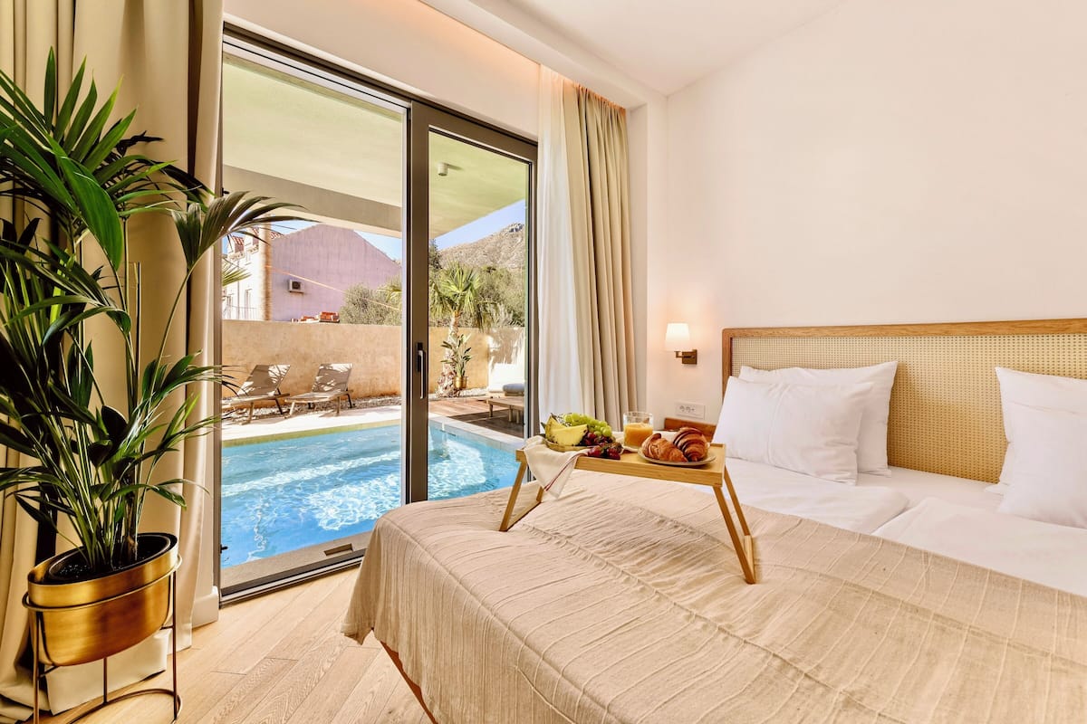 Une chambre d’hôtel avec un lit, un plateau de petit-déjeuner, une plante en pot et une vue sur une piscine.