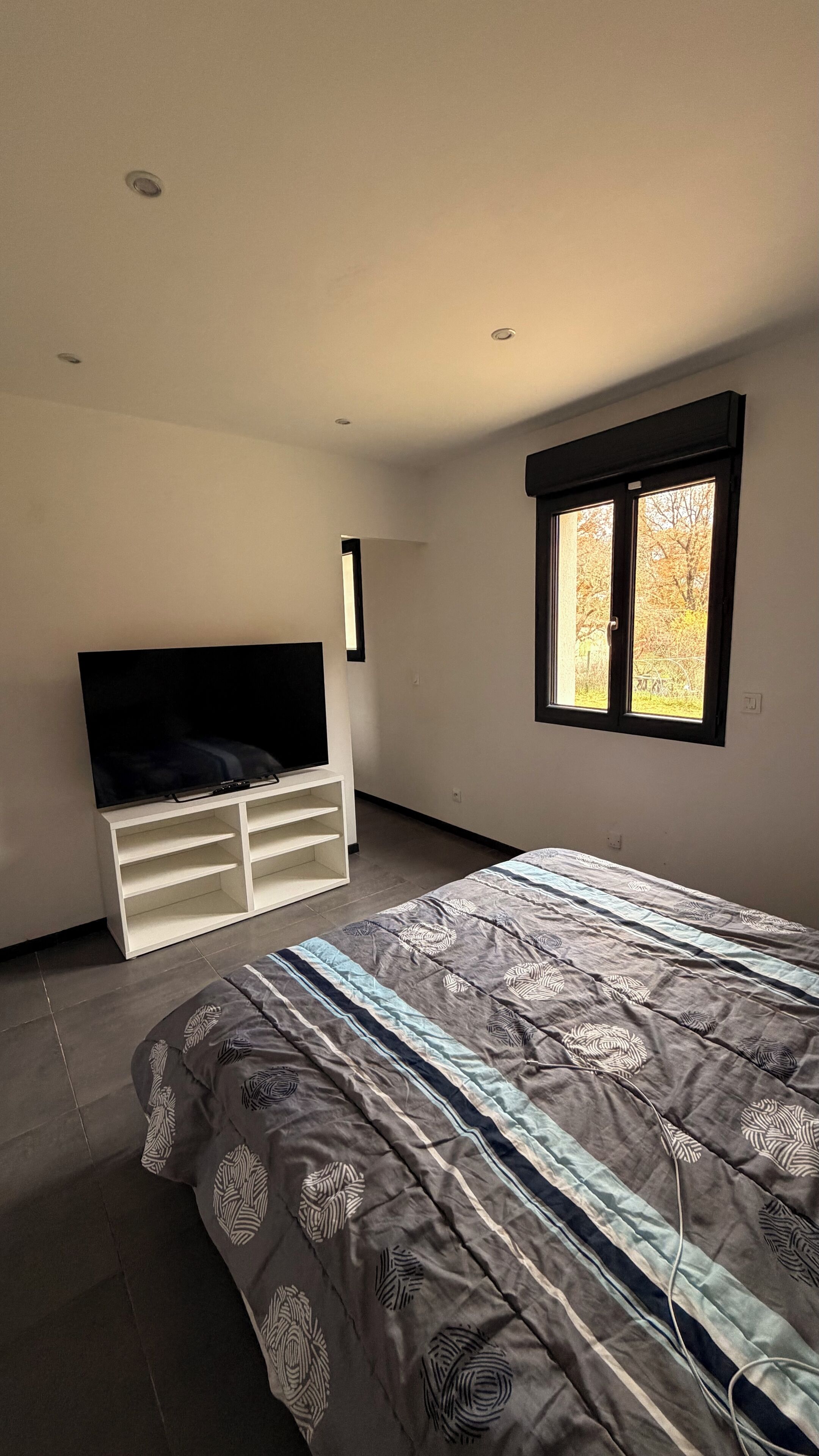 Ein Schlafzimmer mit Bett, Fernseher auf einem Schrank, Fenster und Tür.