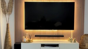Una sala de estar moderna con un televisor de pantalla plana grande montado en una pared de madera, un mueble blanco debajo y un piso de concreto pulido.