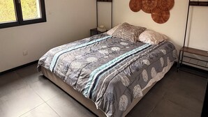 Un dormitorio con cama, una ventana, estante en la pared y una lámpara de techo.