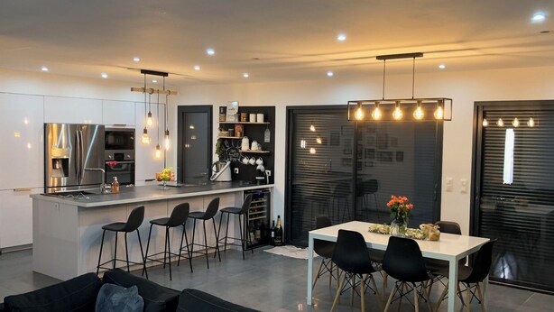 Una cocina moderna con una isla central, taburetes de bar y una mesa de comedor con sillas.