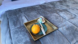 Ein Bett mit einer grauen Decke, ein Tablett mit einer Orange, einer Tasse und einem Löffel.