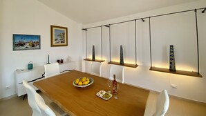 Ein Essbereich mit einem Holztisch, weißen Stühlen, einer Zitronenschale, einer Weinflasche und zwei Bildern an der Wand.