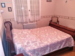 Cozy retreat with a single bed, wooden chair, and radiator, set against a simple backdrop.