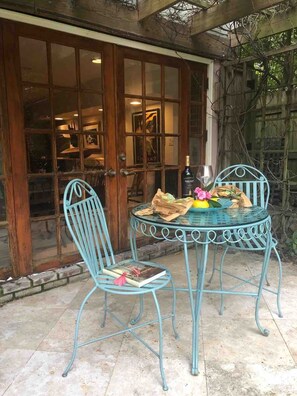 Eine Terrasse mit einem Glastisch und zwei Stühlen, ein Buch auf einem Stuhl und eine Flasche auf dem Tisch.