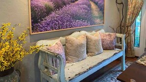 A room with a vintage sofa, a large painting of lavender fields, and a vase with yellow flowers. - La Petite Fleur Rouge | Elegant & Cozy 2/1 Getaway (North Charleston)
