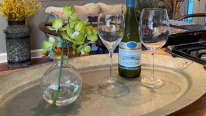 A kitchen counter with a wine bottle, two wine glasses, and a vase with flowers. - La Petite Fleur Rouge | Elegant & Cozy 2/1 Getaway (North Charleston)