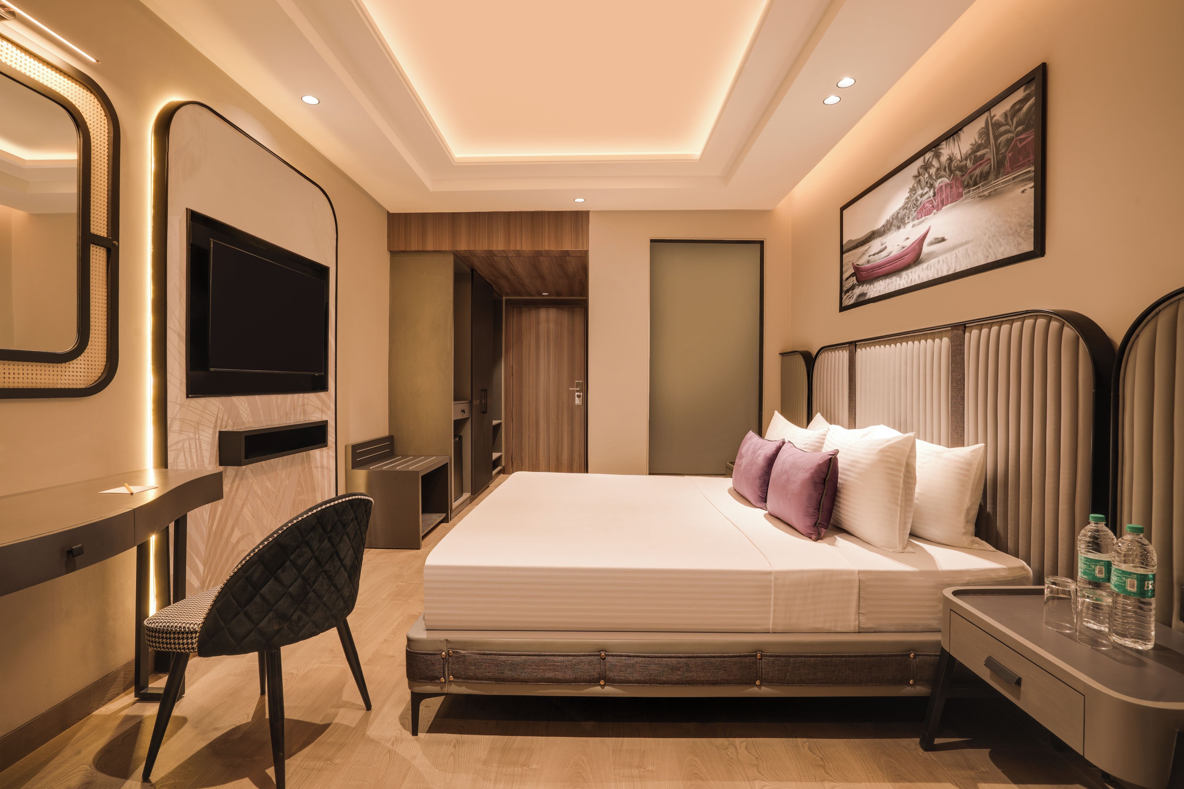 A modern hotel room with a large bed, a desk with a chair, a TV, and a painting on the wall.