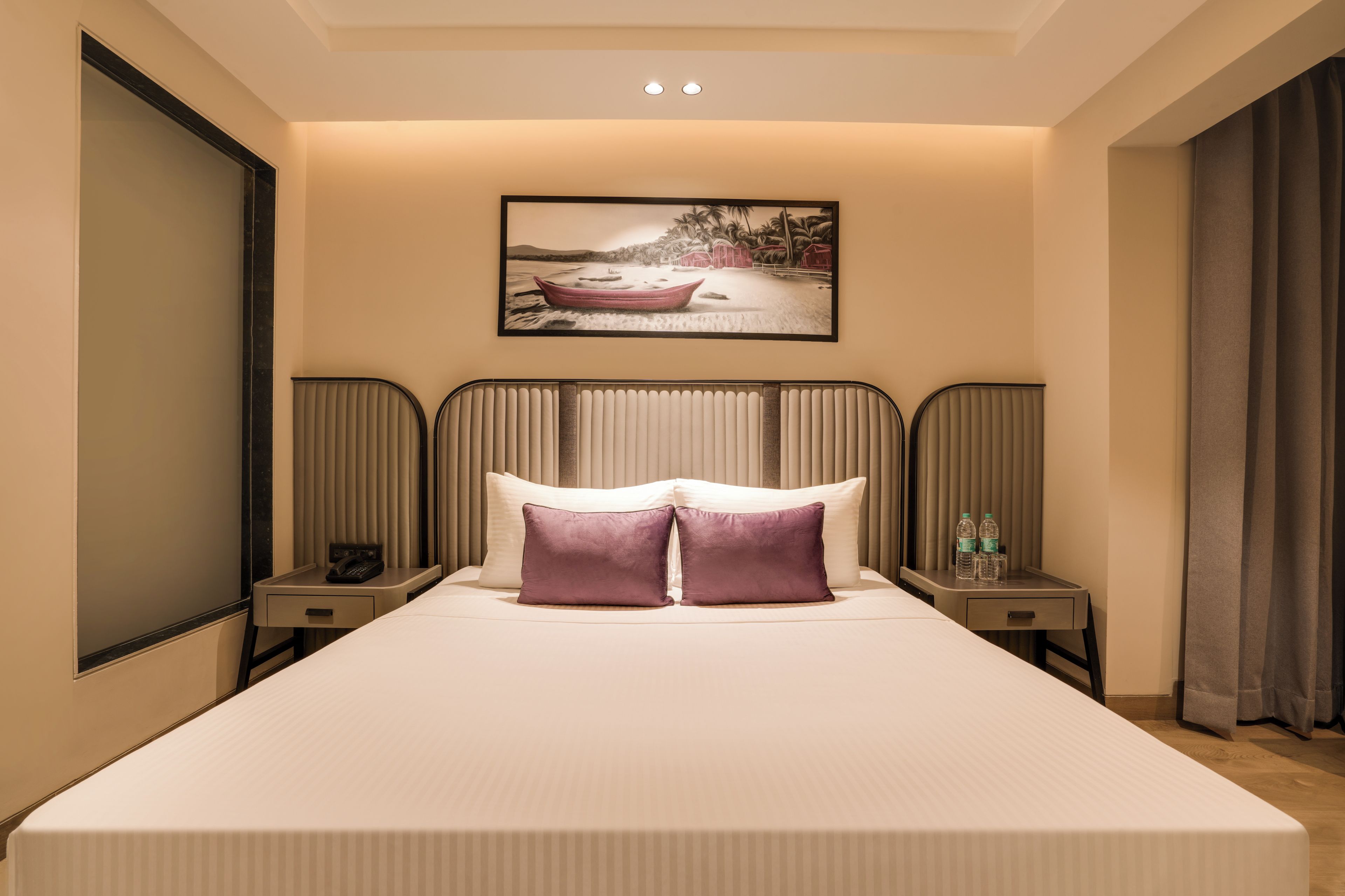 Een hotelkamer met een groot bed, twee nachtkastjes, een hoofdeinde, een schilderij aan de muur en een raam met gordijnen.