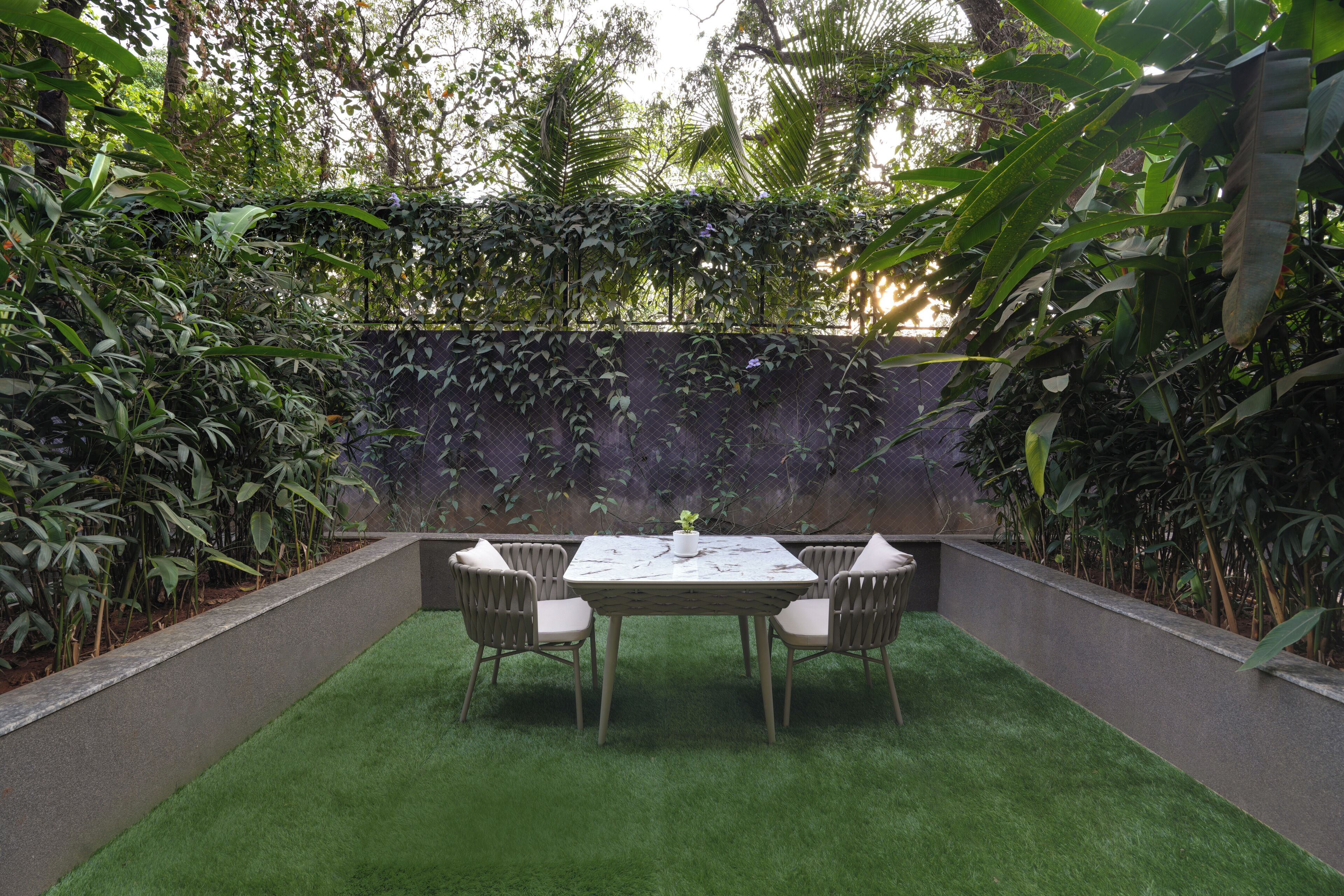 A patio with a table and chairs, surrounded by lush greenery and a stone wall.
