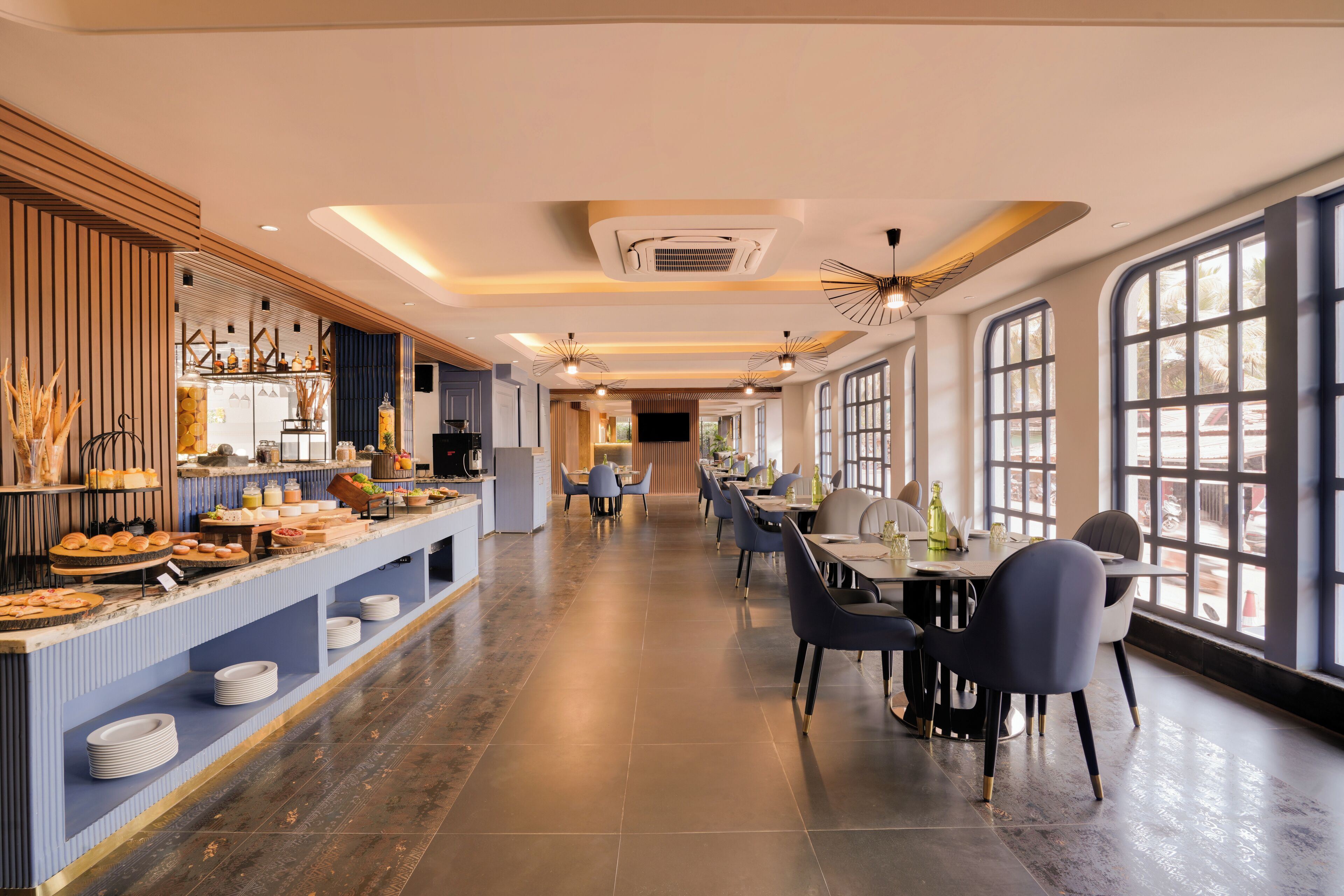 Et moderne spiseområde med en buffet til venstre og et langt bord med stole til højre, store vinduer giver naturligt lys.