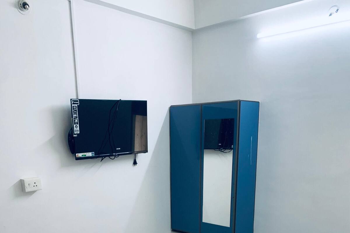 Ένα υπνοδωμάτιο με ένα κρεβάτι, μια μπλε ντουλάπα, μια μικρή τηλεόραση και μια πρίζα.