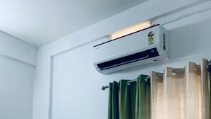 A bedroom with a bed, white walls, an air conditioning unit, and green and beige curtains. - Celestia residency (Kanayannur)