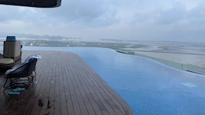 Ein Pool ohne Ende mit einer Holzterrasse, einem Liegestuhl und einem kleinen Tisch.