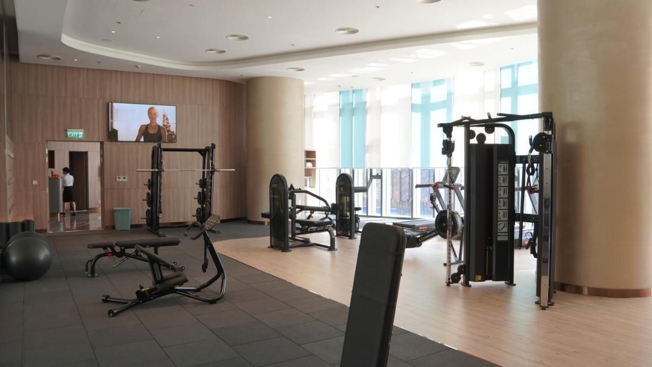 Une salle de sport équipée de divers appareils d’exercice, d’un écran de télévision et d’une grande fenêtre donnant sur l’extérieur.