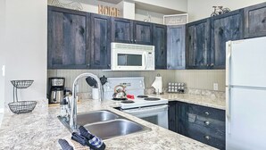 A modern kitchen with dark wooden cabinets, a white microwave, stainless steel sink, and a built-in oven. - Ski-In/Ski-Out Mountain Retreat / Hot Tub + Garage (Panorama)
