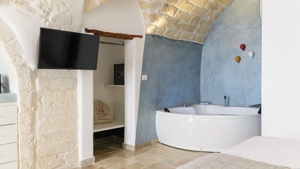 A modern bathroom with a stone wall, a large bathtub, and a flat-screen TV mounted on the wall.