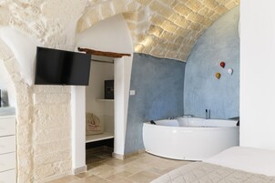 A modern bathroom with a stone wall, a large bathtub, and a flat-screen TV mounted on the wall.