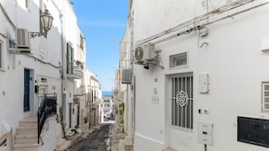 A narrow street with white buildings, air conditioning units, and a blue door.