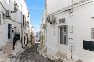 A narrow street with white buildings, air conditioning units, and a blue door.