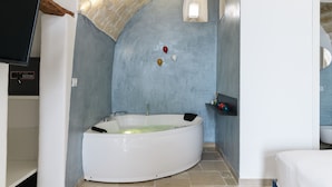 A bathroom with a white bathtub, a television mounted on the wall, and a small window.