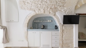 A kitchen with white cabinets, a marble countertop, a built-in sink, and a flat-screen TV mounted on the wall.