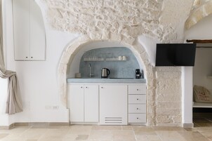 A kitchen with white cabinets, a marble countertop, a built-in sink, and a flat-screen TV mounted on the wall.