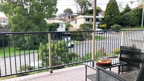 A balcony with a view of a residential street, a potted plant, and outdoor furniture.