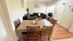 A dining area with a wooden table and chairs, a sofa, a television, and a 'No Smoking' sign on the wall.